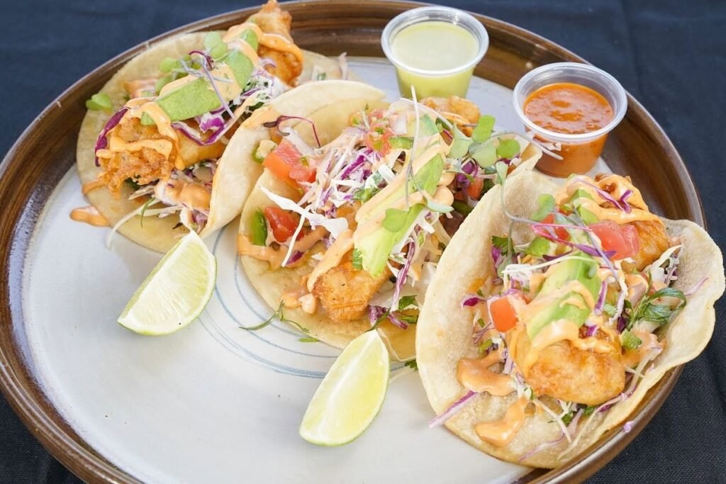 ATOS International Cuisine fish tacos topped with avocado, cabbage and sauce, served with lime wedges