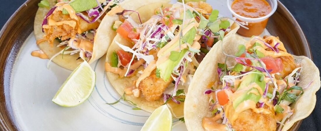 ATOS International Cuisine fish tacos topped with avocado, cabbage and sauce, served with lime wedges