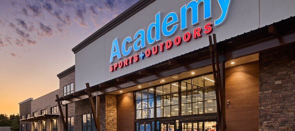 Academy Sports + Outdoors storefront with illuminated signage at dusk.