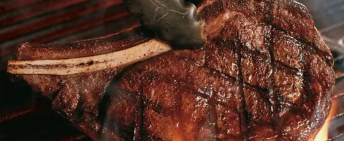 LongHorn Steakhouse bone-in steak cooking over flames on a grill.