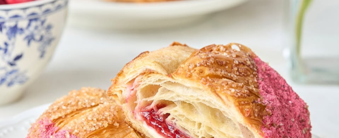 Maman croissant cut open to show red fruit filling and cream beneath flaky pastry layers.