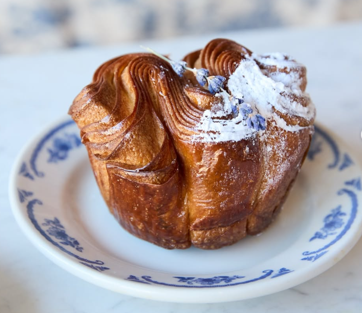 Maman layered golden pastry with powdered sugar on a blue-and-white plate.