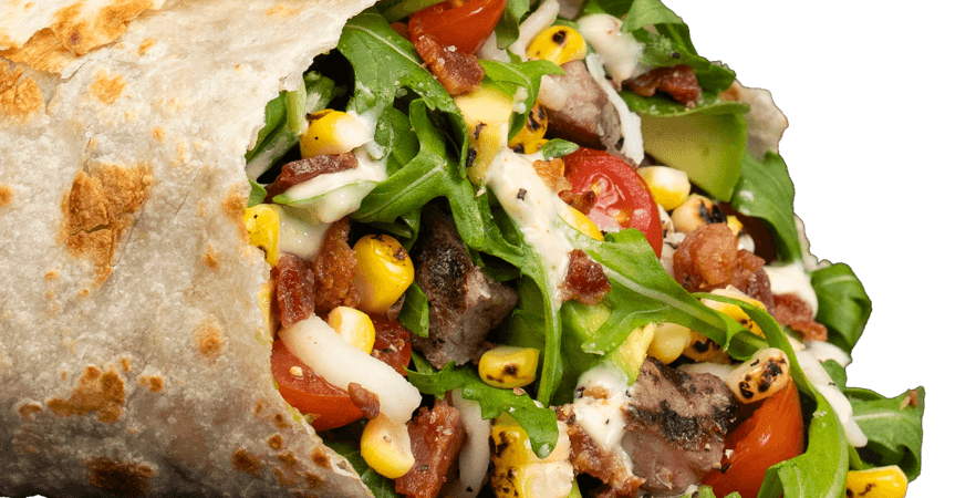 Piada flatbread wrap filled with meat, greens, tomatoes, corn, and sauce.