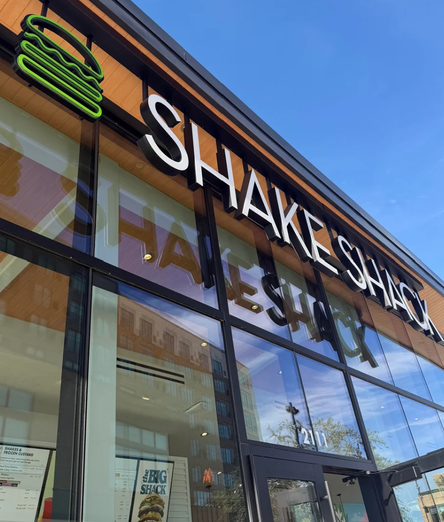 Shake Shack storefront with white lettering, a green burger logo, and glass windows.