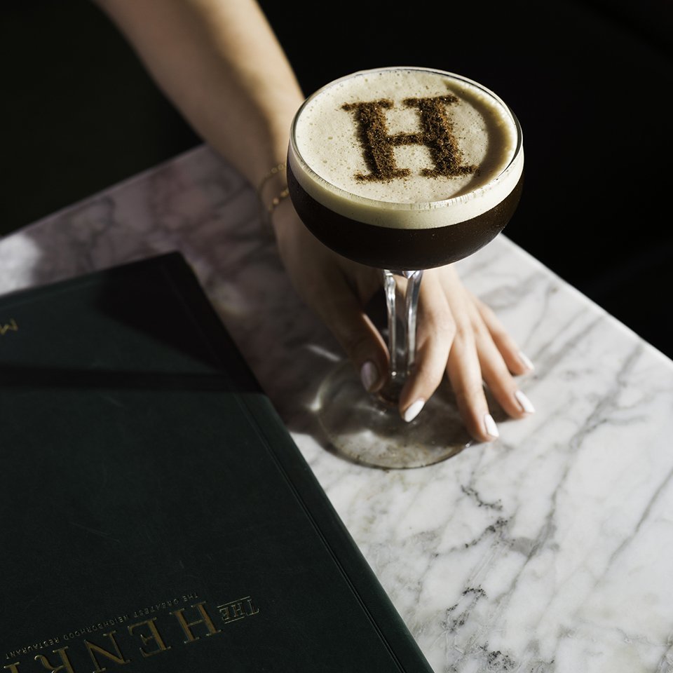 Foam-topped cocktail with an H garnish at The Henry.