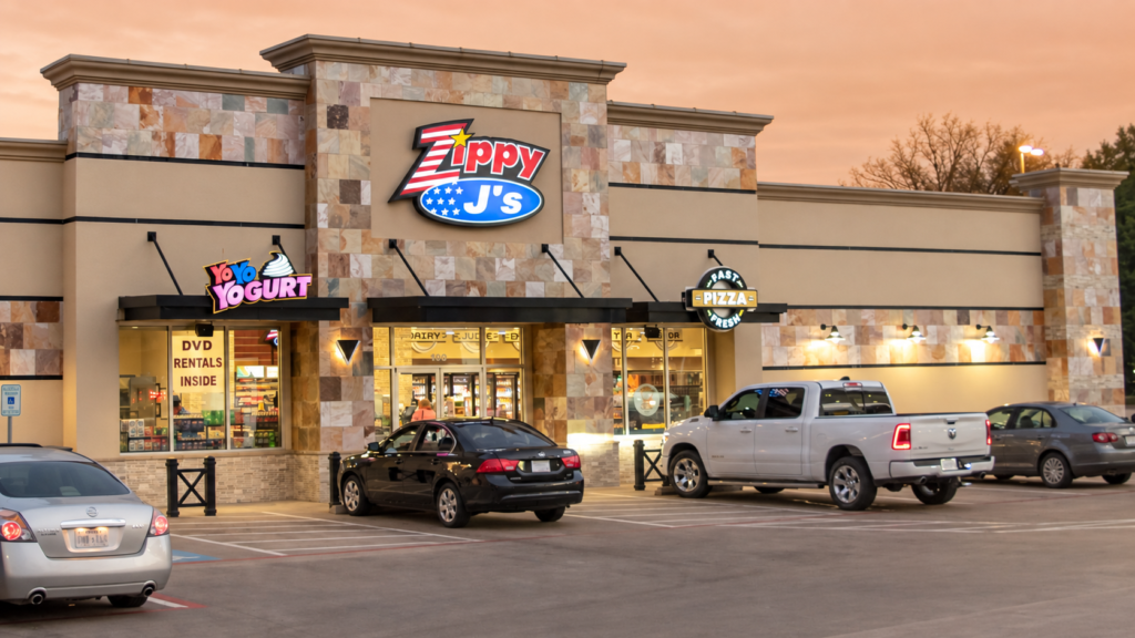Zippy J’s convenience store exterior with illuminated signage and vehicles parked outside at dusk