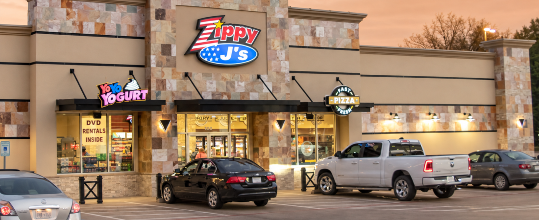 Zippy J’s convenience store exterior with illuminated signage and vehicles parked outside at dusk