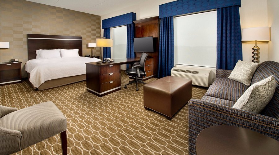hamptoninnsuiteskingstudio Hampton Inn & Suites guest room with a king bed, desk and seating area
