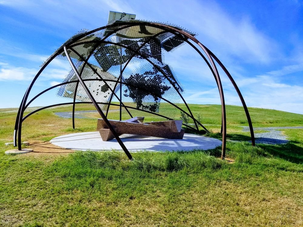Curved metal public art structure with seating on a grassy hill at Pearsall Park.