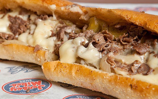 Jersey Mike's cheesesteak sandwich with sliced steak and melted cheese on branded paper.