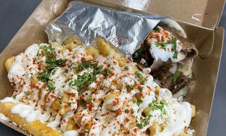 Gyro sandwich and fries topped with sauce and herbs from Stop N Go Gyros