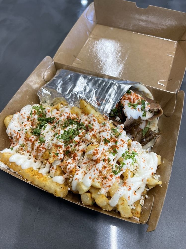 Gyro sandwich and fries topped with sauce and herbs from Stop N Go Gyros