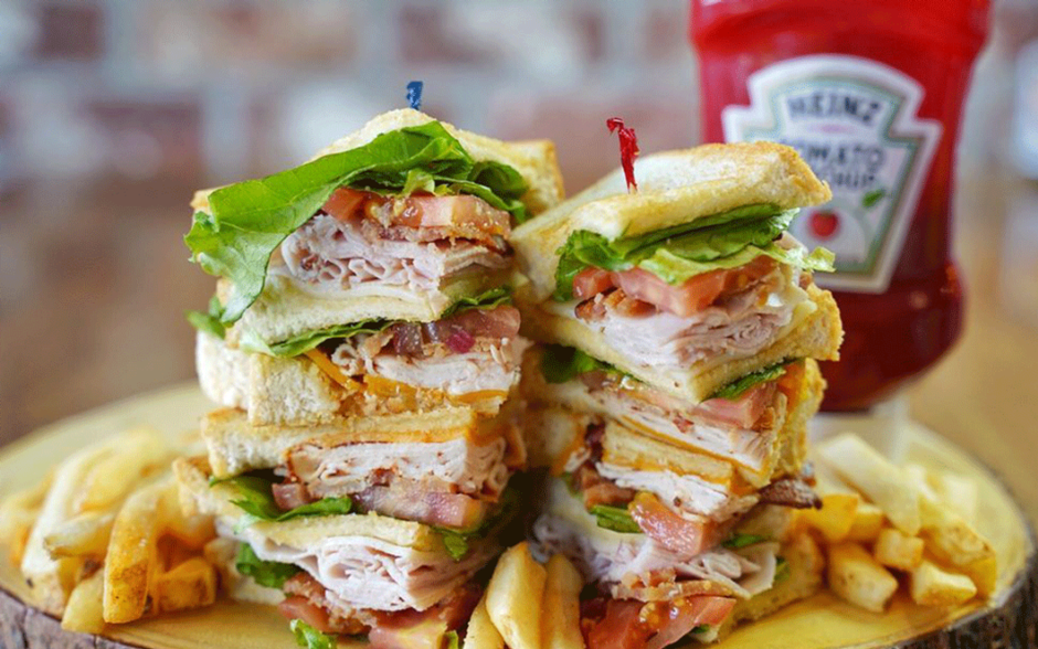The Toasted Yolk club sandwich The Toasted Yolk club sandwich stacked with meat, bacon, lettuce, and tomato beside fries