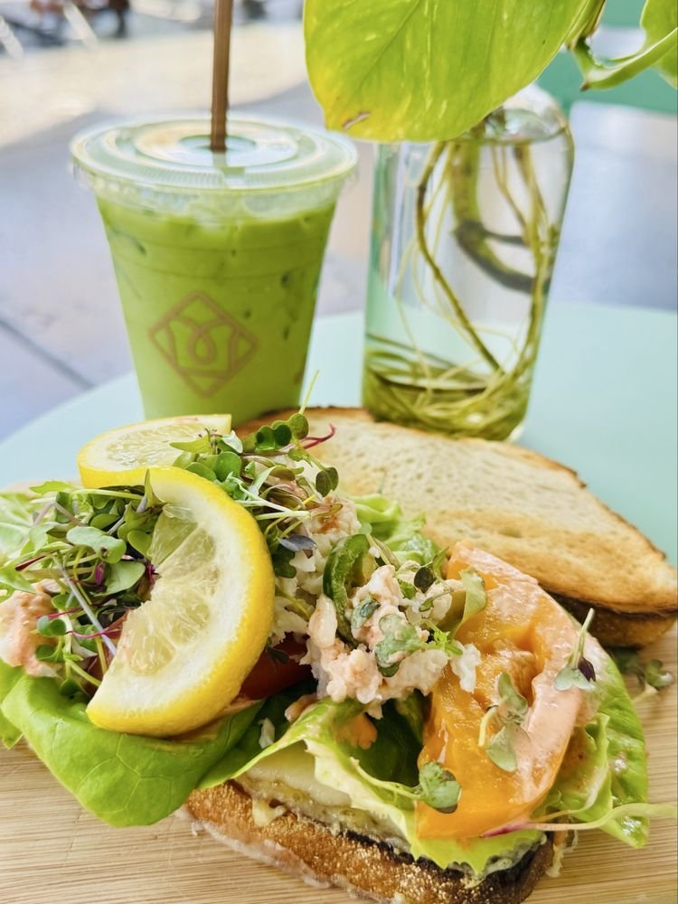 toastique spicycrabtoast Toast with avocado, greens and lemon beside an iced drink, illustrating the Toastique San Antonio cafe concept